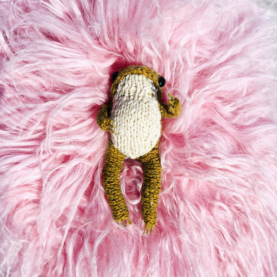 Knitted frog toy on a fluffy pink surface